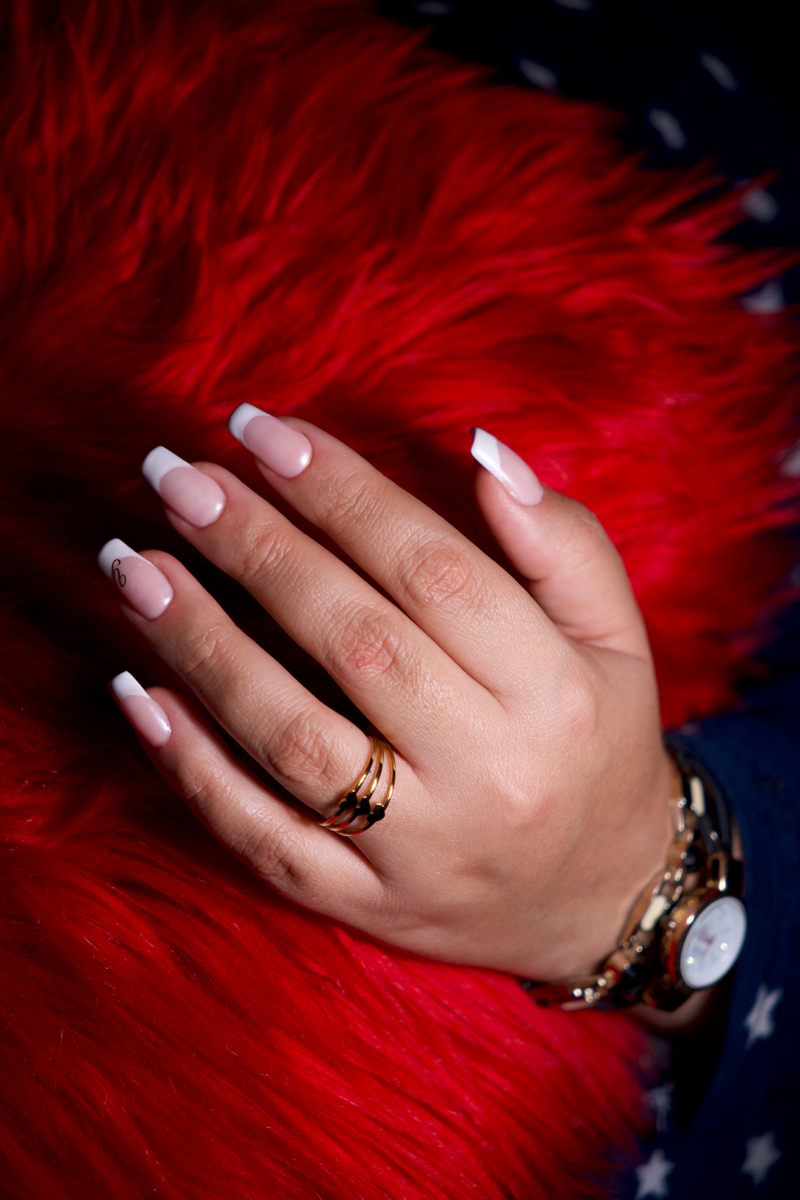 Close-up of a hand with French manicure adorned with rings and a gold watch.